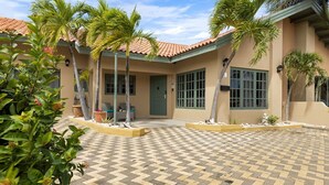 A building with a tiled roof, palm trees, and a checkered pavement. - Cozy 3BR Town Home in Gated Community @ Palm Beach (Noord)