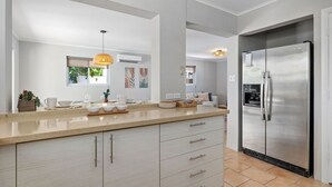 Een moderne keuken met een groot eiland, een koelkast van roestvrij staal en een hangende hanglamp.