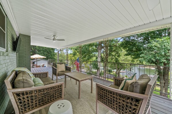 A covered outdoor patio with wicker furniture, a table, and a view of a lake and trees.