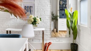 Een moderne woonkamer met een witte bakstenen muur, een witte tafel met een bloevas, een blauwe stoel en een groot raam met uitzicht op een stenen gebouw.