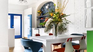 Een moderne keuken met witte kasten, een blauwe deur en een eethoek met een witte tafel en rode en witte stoelen.