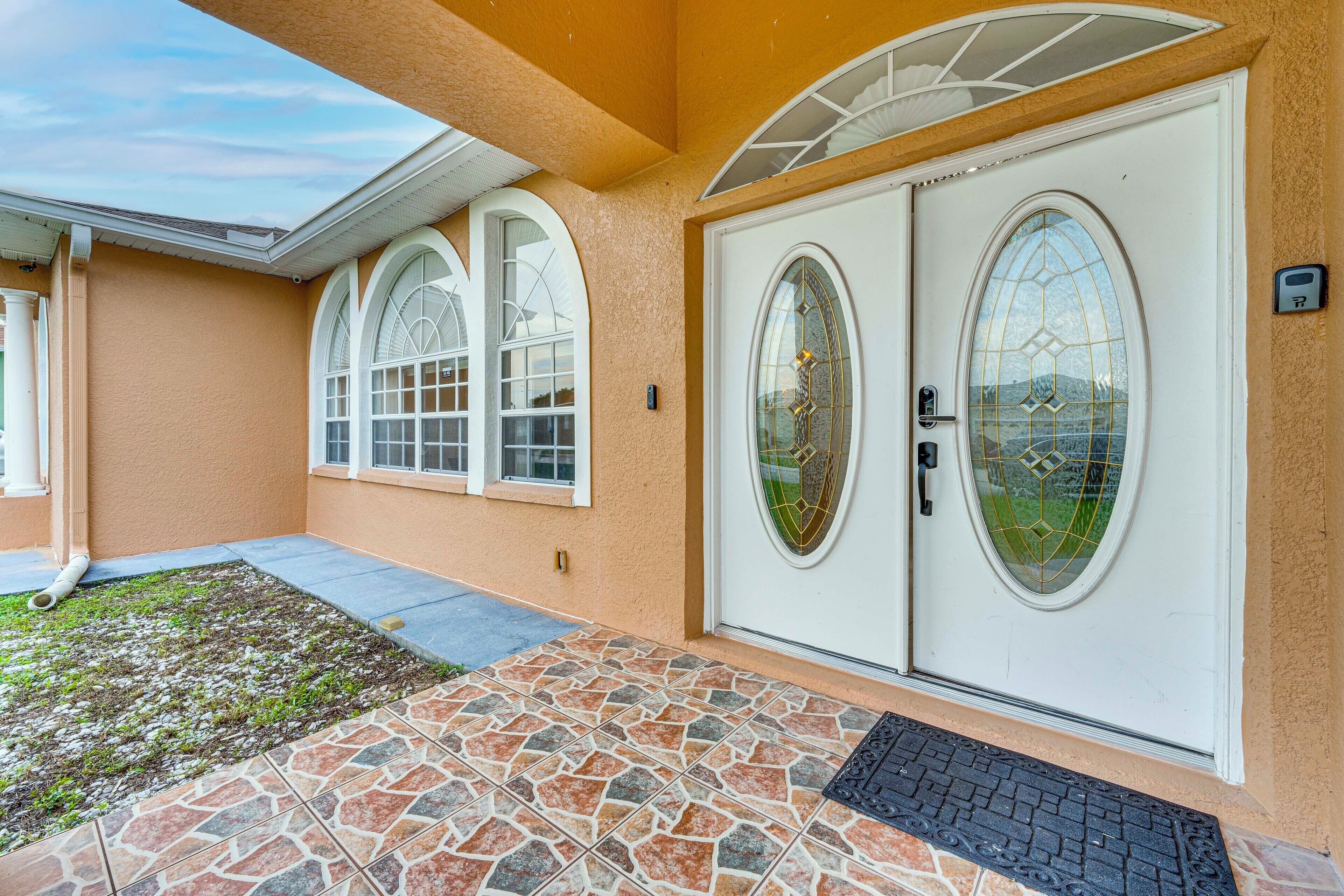 Una casa con entrada de piedra, una puerta blanca con panel de vidrio y un pequeño jardín.