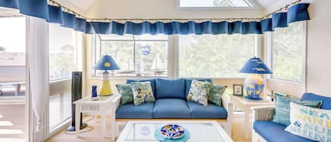 A room with a blue sofa, white coffee table, and a view of the outdoors.