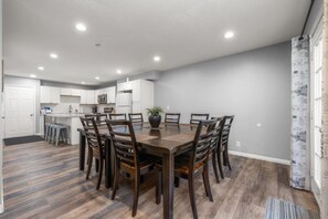 A modern kitchen with white cabinets, a central island, and a dining area with a wooden table and chairs. - Oak Ridge Retreat | Hot Tub | Grill | Spacious (Cottonwood Heights)