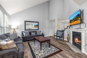 A modern living room with a sofa, coffee table, fireplace, and a TV mounted on the wall. - Oak Ridge Retreat | Hot Tub | Grill | Spacious (Cottonwood Heights)