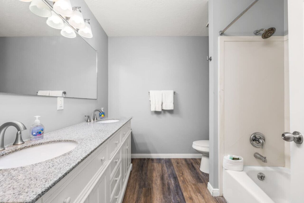 A bathroom with a double sink vanity, a large mirror, a towel rack, a toilet, and a shower area.