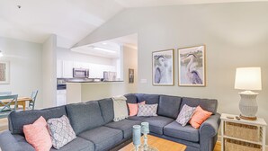 Een woonkamer met een grijze modulaire bank, een salontafel met decoratieve voorwerpen, een lamp en een aan de muur bevestigde televisie.