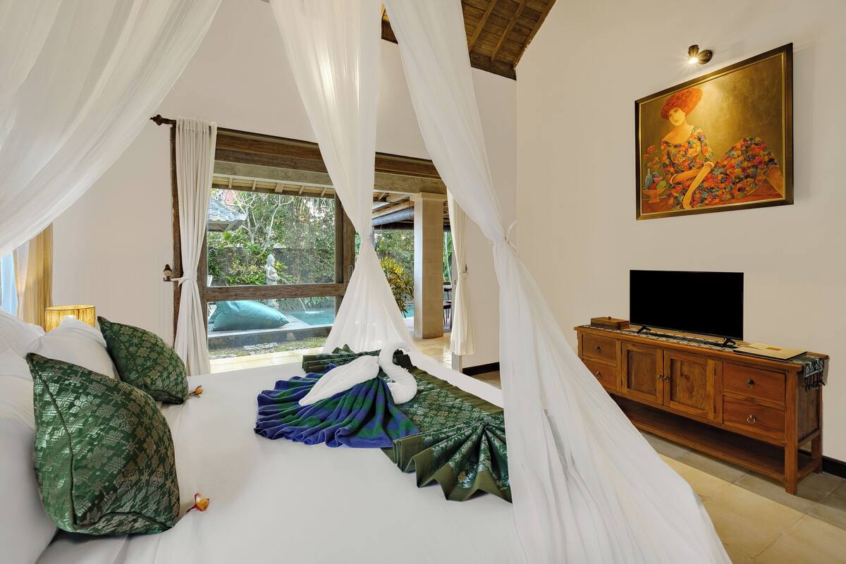 A bedroom with a canopy bed, a wooden dresser, and a painting on the wall.