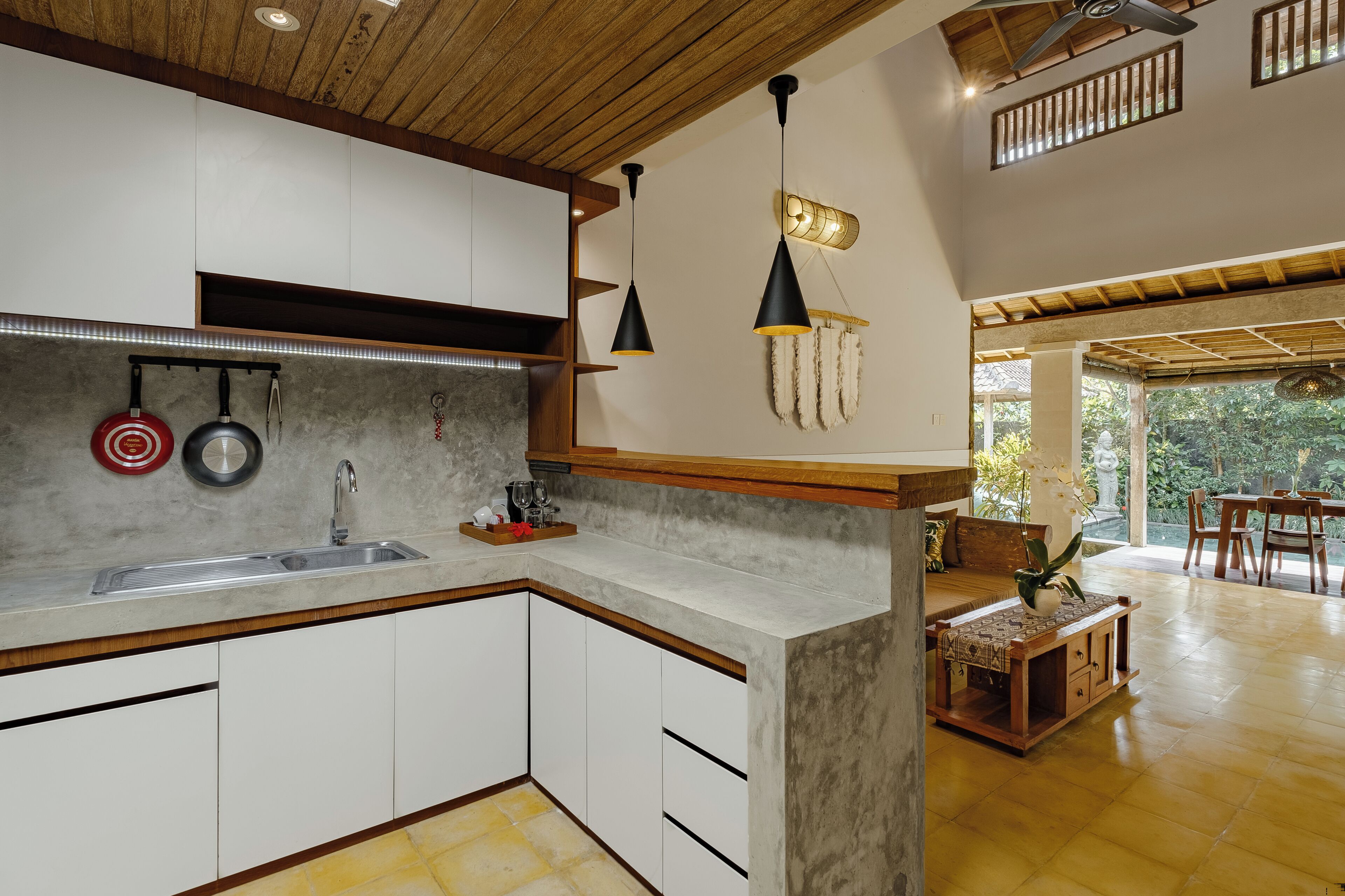 A modern kitchen with white cabinets, a granite countertop, and a built-in sink. There are hanging pots and a small island with a plant.
