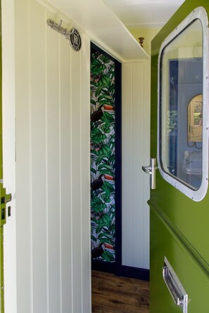 Un pasillo estrecho con una puerta decorada con papel tapiz tropical y un ventanal pequeño.