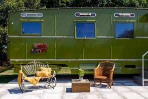 Una caravana verde con una cama, una silla de mimbre y una pequeña mesa con una planta.