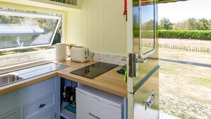 A compact kitchen with a sink, a toaster, and a refrigerator. There is a window with a view of a garden. - Restored Showman's Carriage, King Bed and Pool (Batchmere)