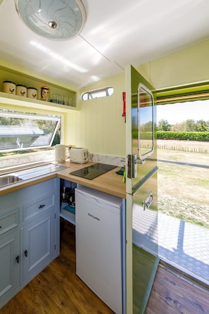 Cocina compacta con lavamanos, tostadora y refrigerador. Se observa una ventana con vista a un jardín.