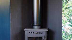 A wood-burning stove in a corner of a room with a dark wall and a wooden floor.