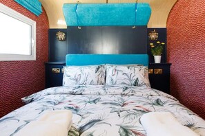 Ein Schlafzimmer mit einem blumigen Bettüberwurf, einem blauen Kopfteil und einer dekorativen Wandverkleidung.