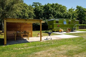 Un véhicule récréatif vert doté d’un patio couvert, d’un barbecue et de sièges d’extérieur.