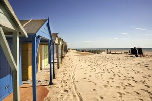 Una hilera de cabañas de playa frente a una arena y el mar al fondo.
