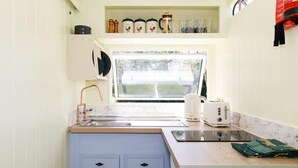 A compact kitchen with a window, a sink, a toaster, and a countertop with jars.
