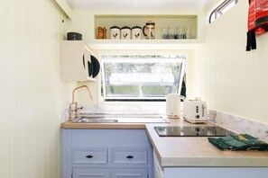 Una cocina compacta con ventana, un lavamanos, un tostador y una encimera con frascos.