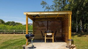 A covered outdoor area with a barbecue grill, a table with chairs, and a trash can.