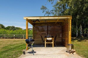 Un espacio al aire libre cubierto con una parrilla, una mesa con sillas y un cubo de basura.