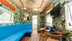 A room with a blue sofa, wooden dining table, chairs, and tropical wallpaper.