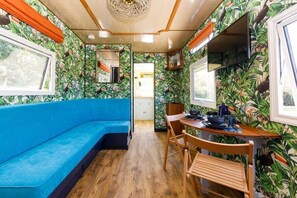Una habitación con sofá azul, mesa de comedor de madera, sillas y papel tapiz tropical.