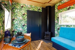 Una habitación acogedora con una mesa de comedor de madera, un sofá azul, una estufa negra y una puerta con estampado tropical.