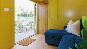 A room with a blue sofa, yellow walls, a wooden ceiling, and a sliding glass door leading to an outdoor area with chairs and a table. - Beautifully Restored WW2 Carriage - Sleeps 6 (Batchmere)
