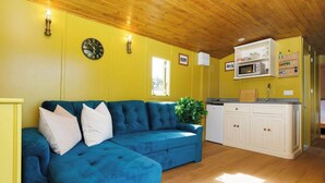 A room with a blue sofa, wooden ceiling, yellow walls, a white cabinet, and a microwave. - Beautifully Restored WW2 Carriage - Sleeps 6 (Batchmere)