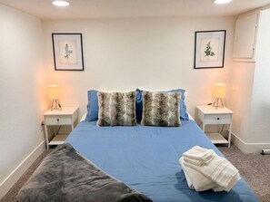 A bedroom with a bed, two nightstands, two wall-mounted lamps, and two framed pictures.