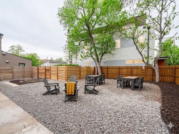 Un jardin avec une terrasse en gravier, une clôture en bois et du mobilier d’extérieur.