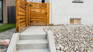A concrete staircase leading to a wooden gate, surrounded by a gravel area and a white building with a window. - Spacious 2BR Garden Suite in Denver Highlands (Denver)