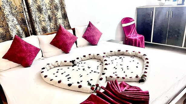 A bed with a white sheet, two pink pillows, a white and black patterned blanket, and a red throw blanket.
