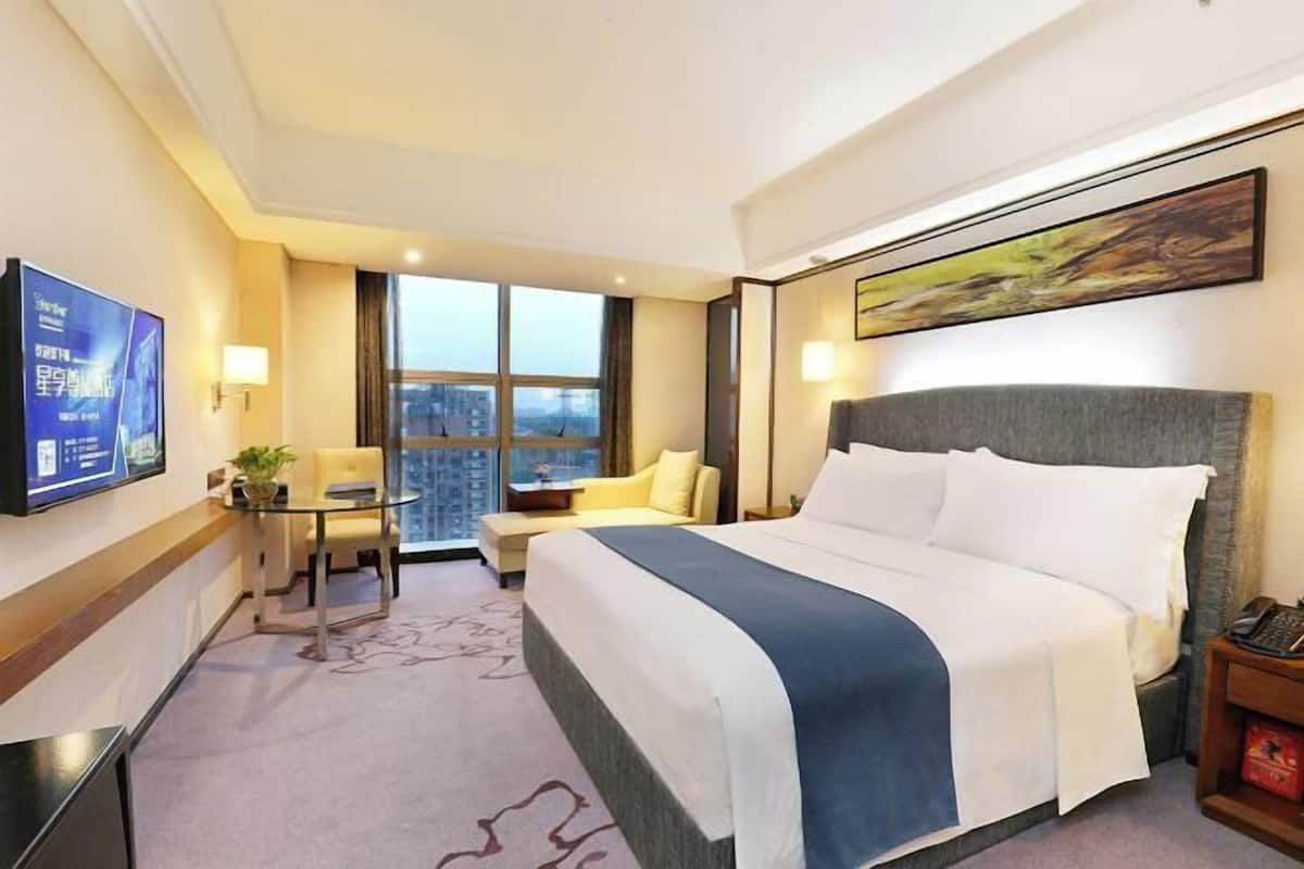 A hotel room with a large bed, a desk with a chair, a television, and a window with a city view.
