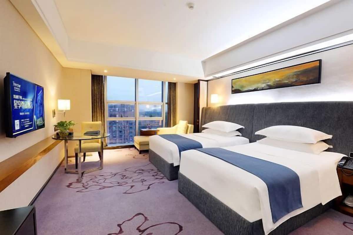 A hotel room with two beds, a TV, a desk, and a large window.