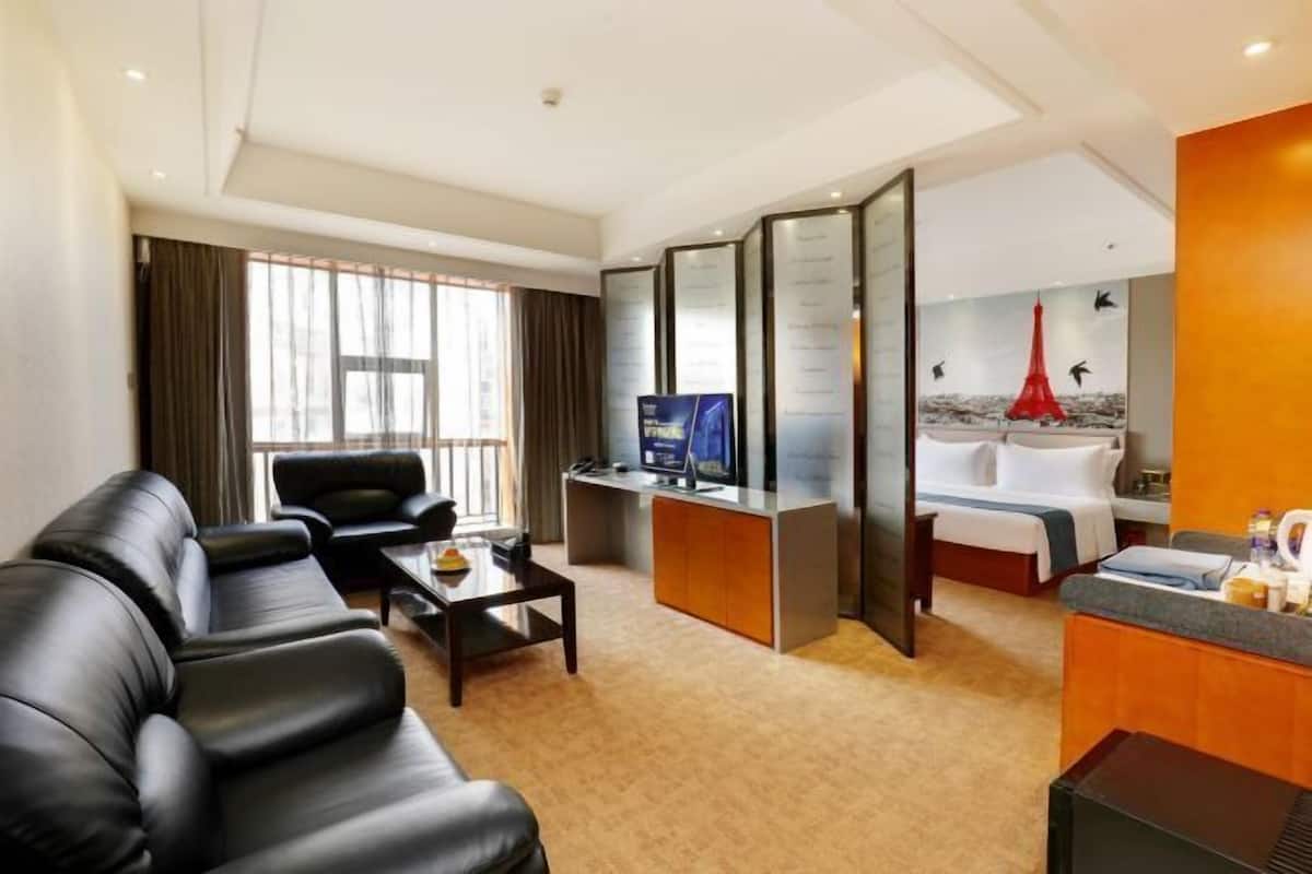 A hotel room with a living area, a desk, a bed, and a bathroom.
