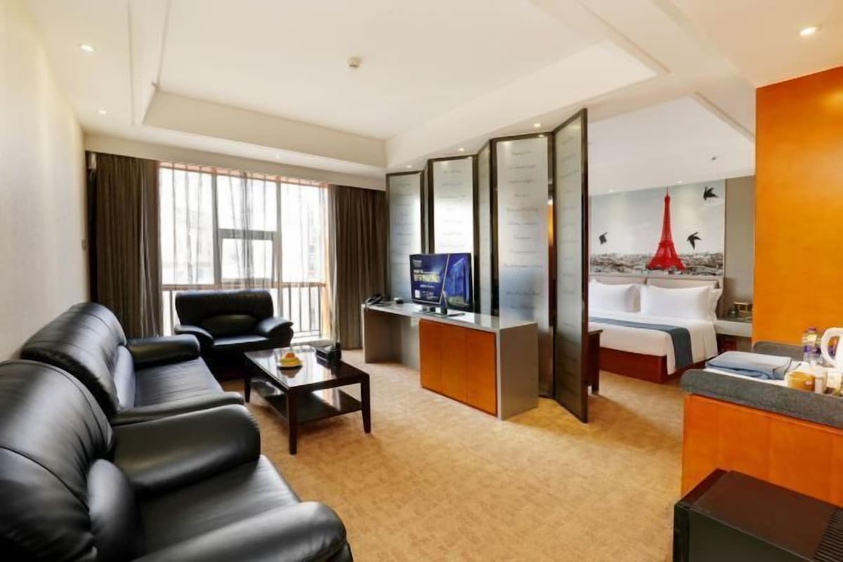 A hotel room with a sofa, a desk, a bed, a TV, and a large window.