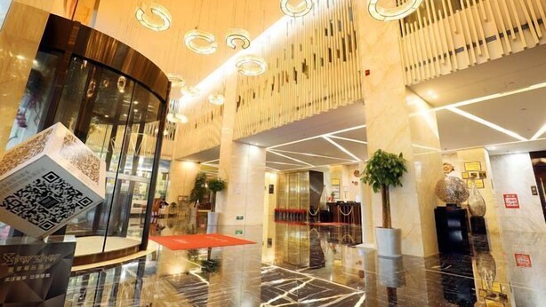Un hall d’hôtel moderne avec un comptoir d’accueil en verre, un espace détente rouge et une plante décorative.