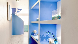 Un interior azul y blanco con una escalera curva, suelo de mármol y estanterías con objetos decorativos.