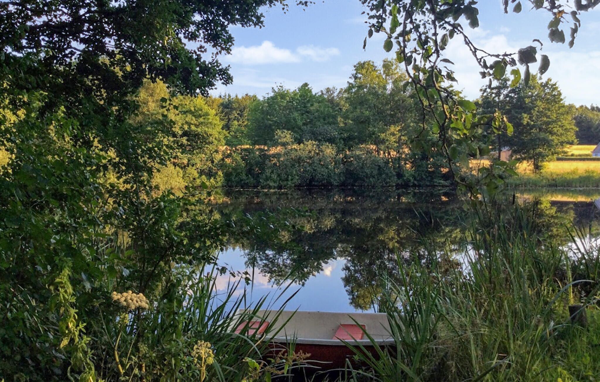 Una vista serena de un lago con un bote amarrado cerca de la orilla, rodeado de exuberante vegetación y árboles que se reflejan en la superficie tranquila del agua.