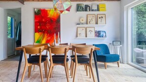 Ein Essbereich mit einem Holztisch und Stühlen, einem farbenfrohen abstrakten Gemälde sowie gerahmten Pflanzenbildern an der Wand.