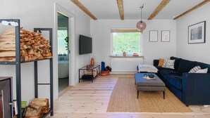 Ein modernes Wohnzimmer mit einem dunkelblauen Sofa, Holzboden, Fernseher und einem Fenster mit Blick auf Grünflächen.