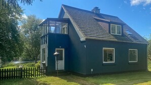Ein dunkelblaues Haus mit geneigtem Dach, einer kleinen Veranda und einem Fenster.