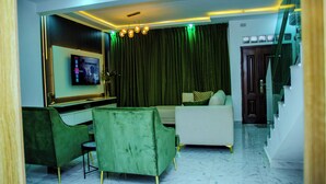 A modern living room with a flat-screen TV, green velvet chairs, a white sofa, and a staircase. - 3 Bed Home Sleeps 6 - Garden, Parking, Wifi (Ibadan)