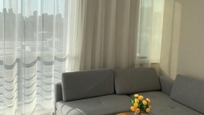 A modern living room with a grey sofa, sheer curtains, and a vase of yellow flowers. - Vienna International Hotel (Xi'an Bell and Drum Tower Ximen Airport Bus) (Xi'an)