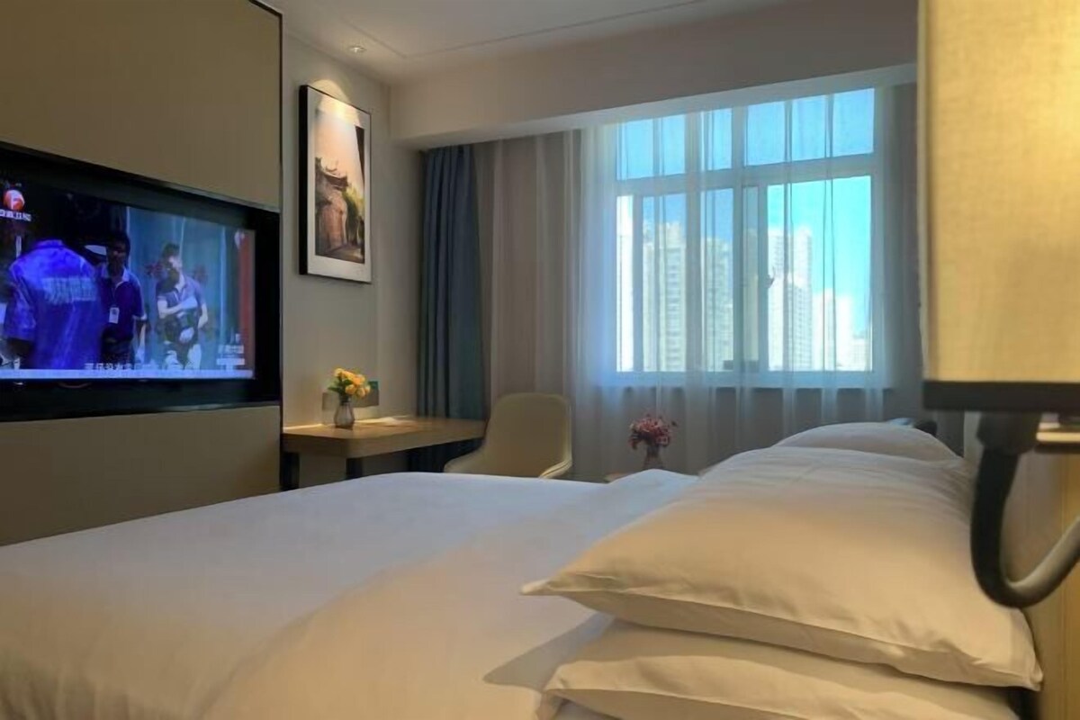 Habitación de hotel con cama, televisión, escritorio, silla y ventana con cortinas.