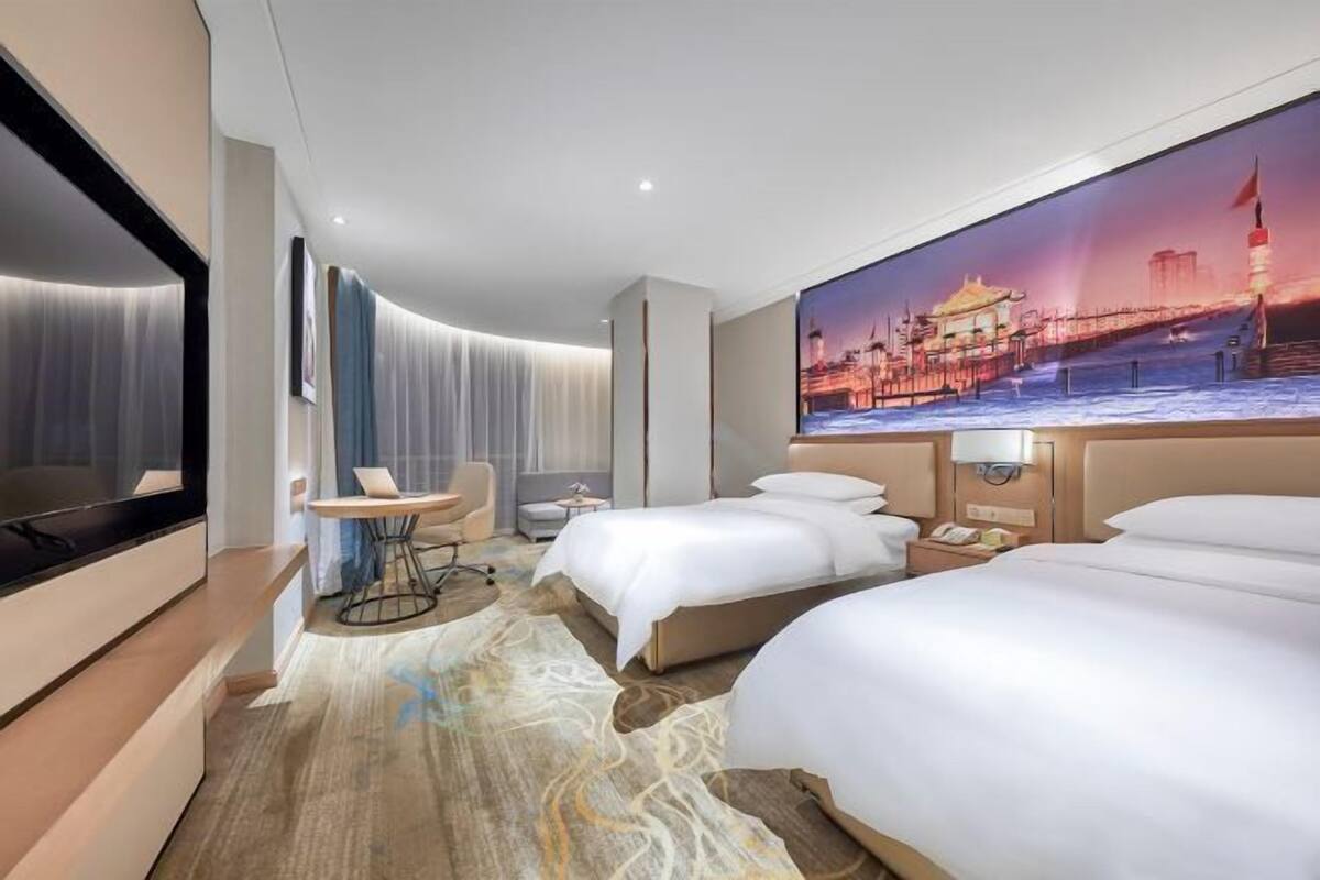 A hotel room with a large bed, a desk, a chair, a TV, and a painting of a cityscape.
