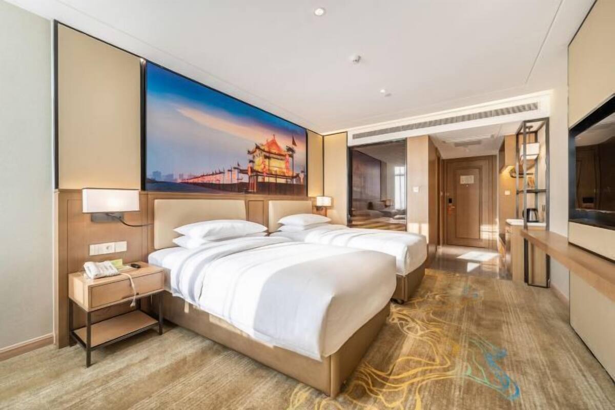 A hotel room with a large bed, bedside tables, a painting, and a TV.