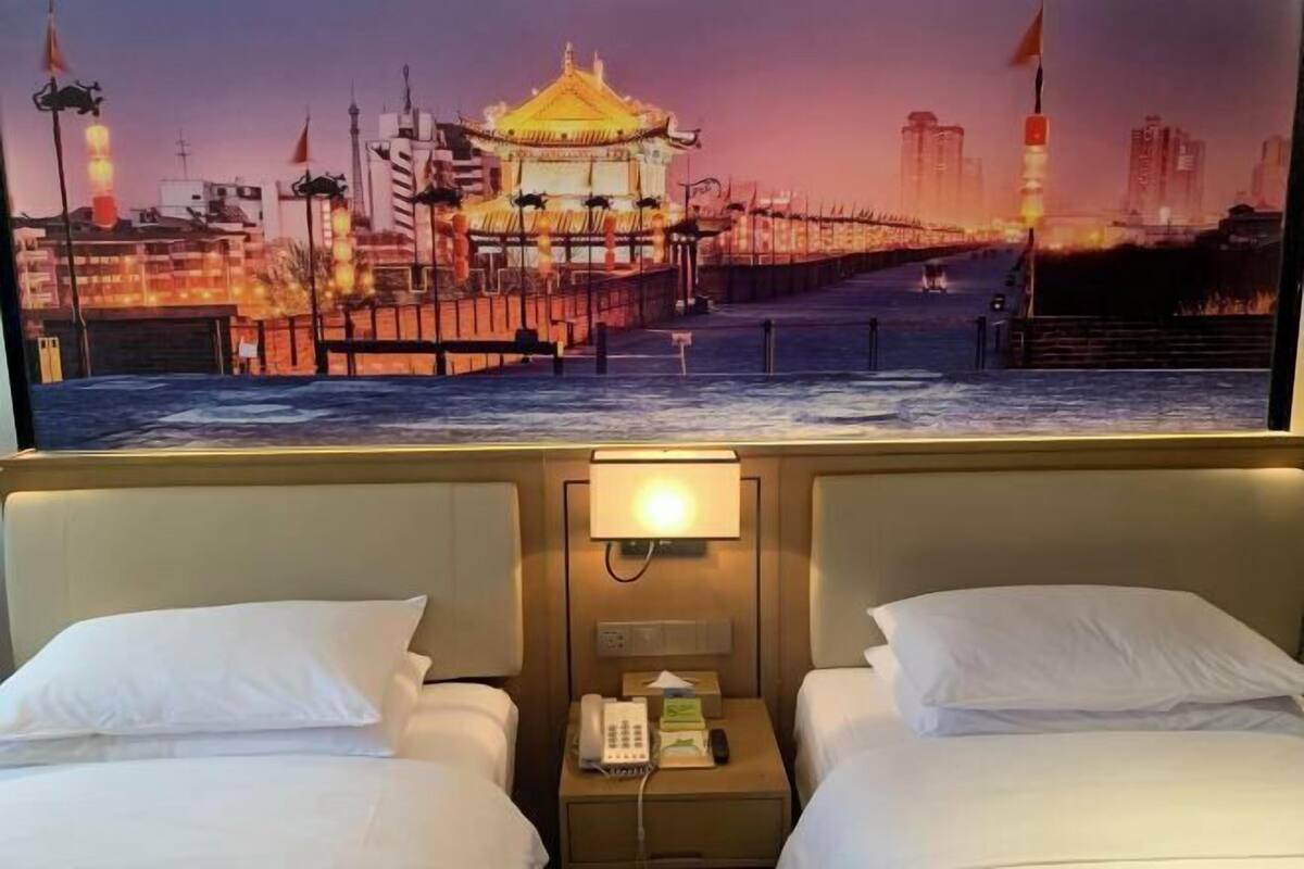 A hotel room with two beds, a nightstand with a phone and tissues, and a cityscape view on the wall.